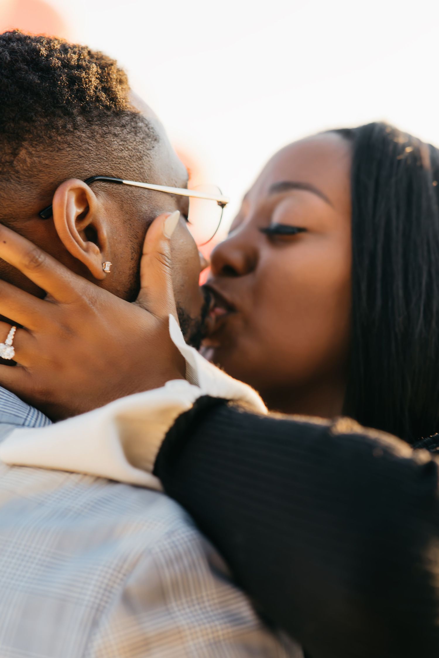 A romantic couple shares an intimate kiss in warm sunlight during what appears to be an engagement photo session.