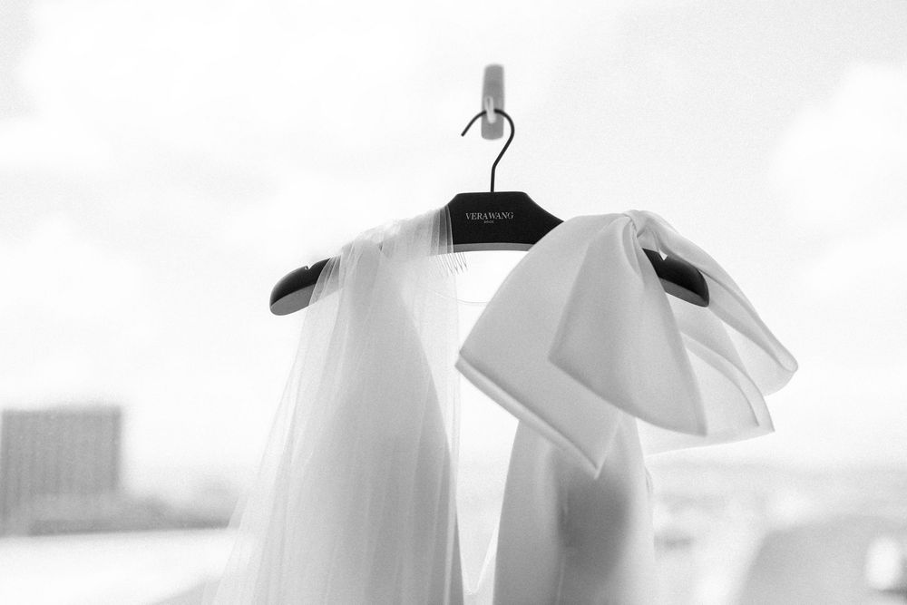 A white button-down shirt hangs elegantly on a black hanger against a light background in black and white.