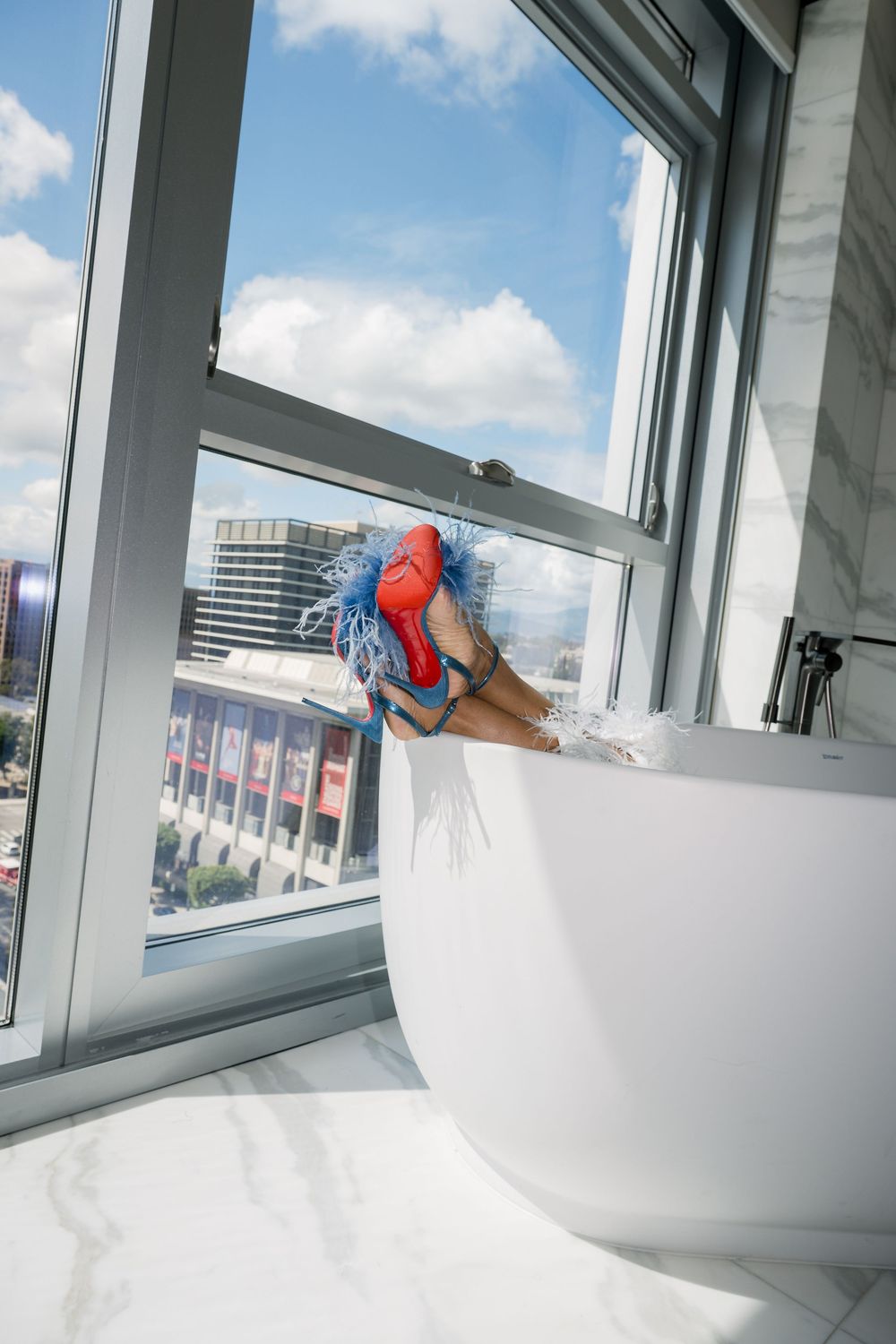 High-rise window view with blue and red cleaning supplies on white windowsill against blue sky and city backdrop.