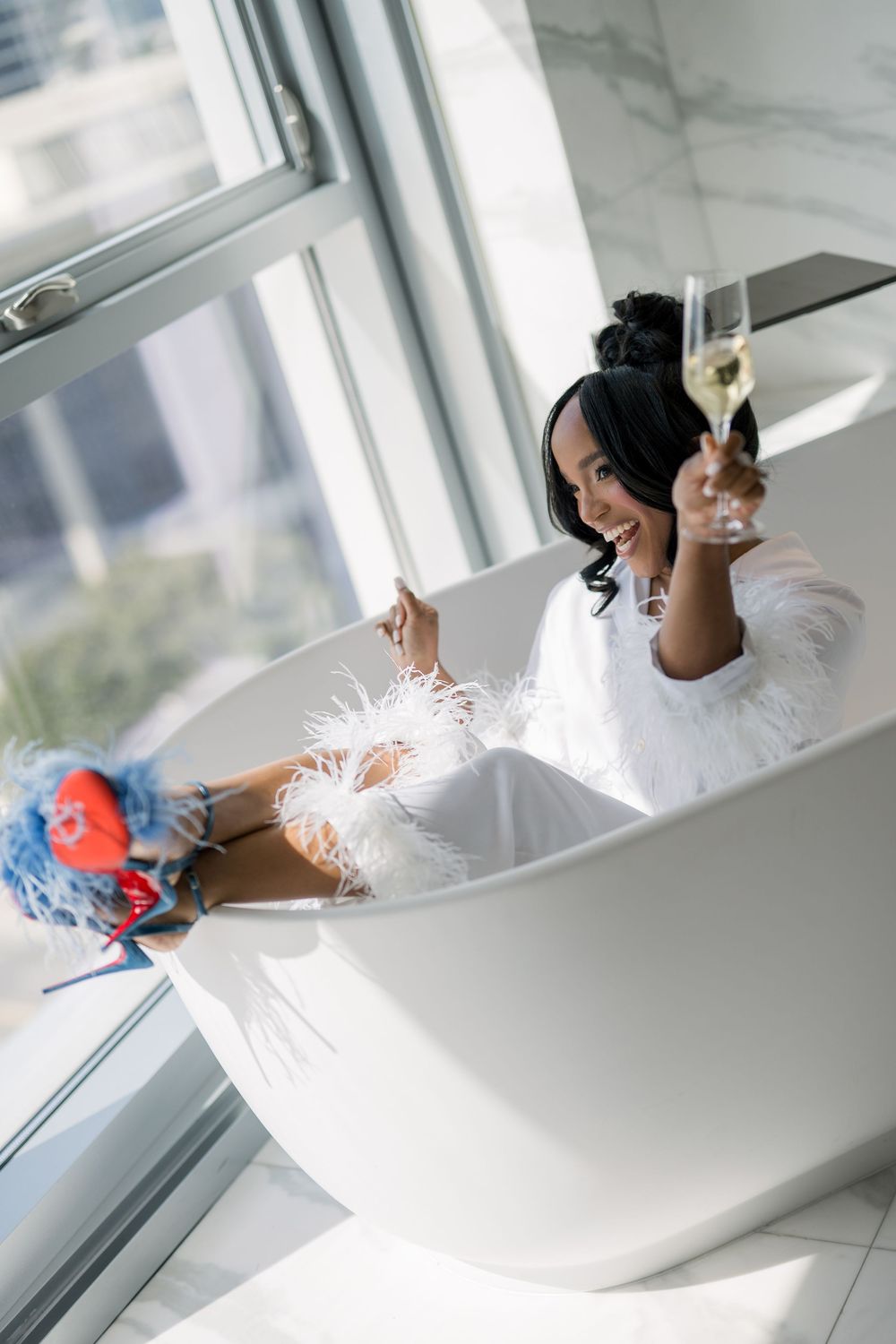 Happy woman in white robe relaxing in bathtub with champagne glass.