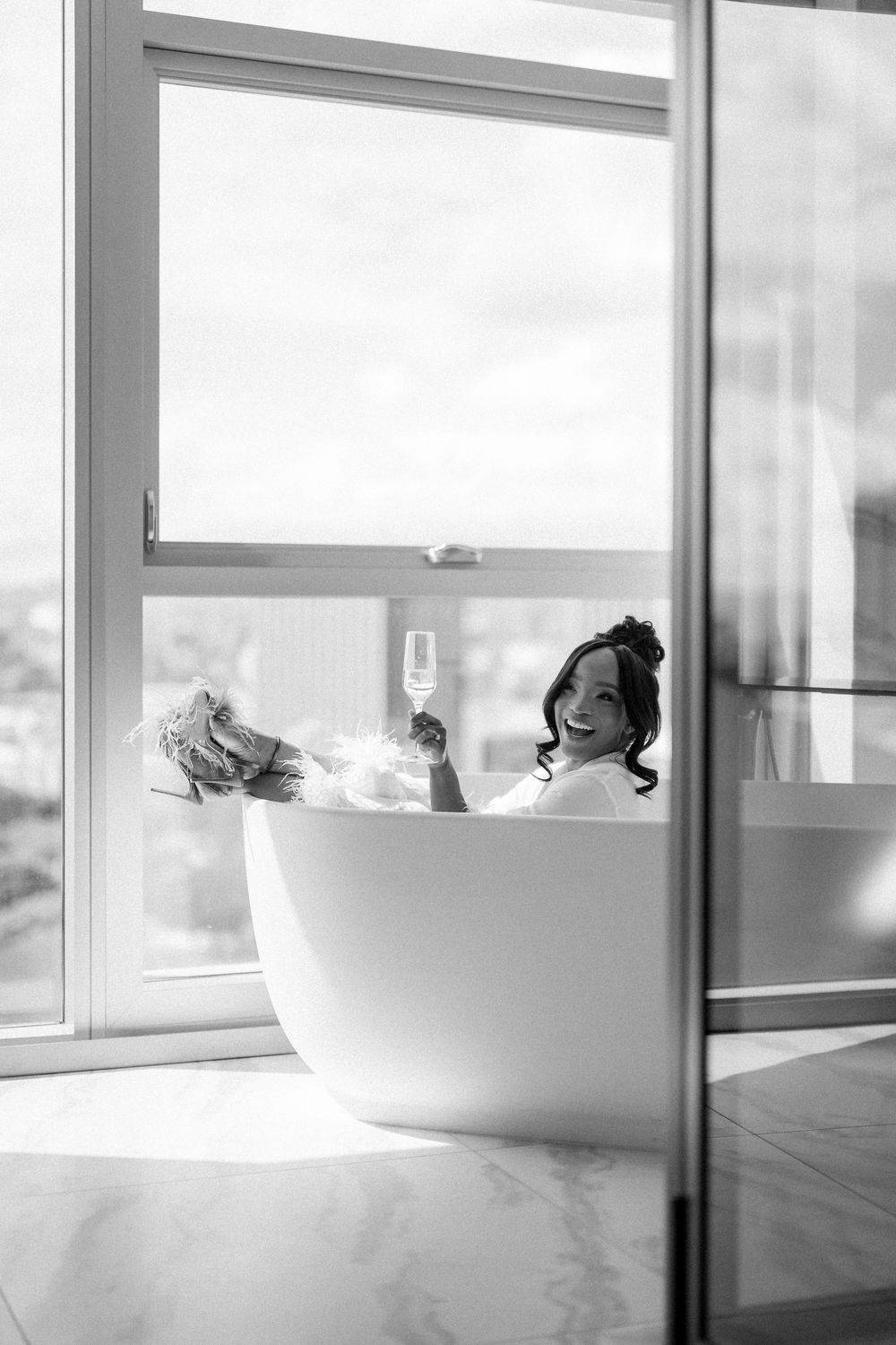 A relaxing scene in a freestanding bathtub with champagne glass against a bright window view.