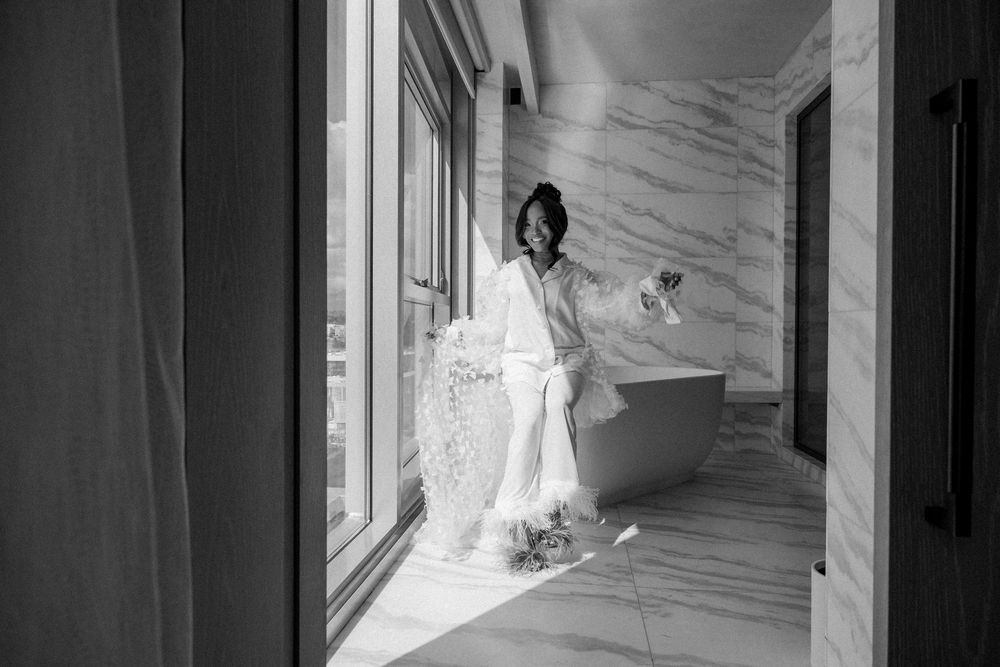 Black and white photo of someone in a white robe standing in a modern marble hallway with large windows.