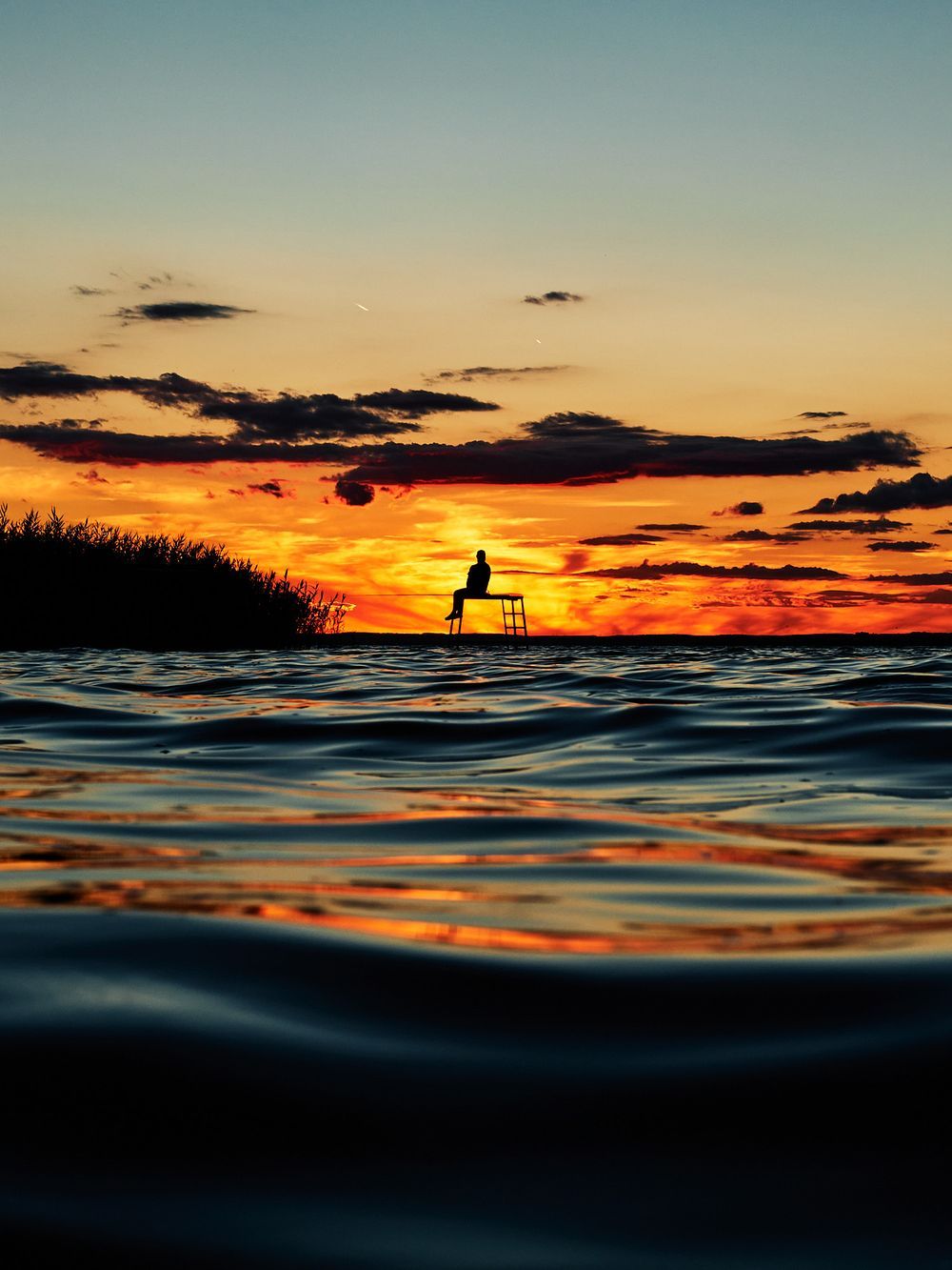 Silhouette of a lifeguard tower against a dramatic orange sunset sky with rippling ocean waters in the foreground.