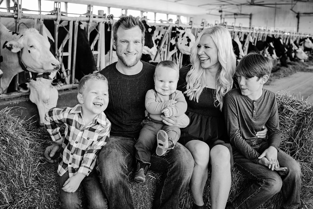 Black and white photo of family of five sitting on hay bales in a dairy barn.