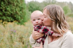 Blonde mother tenderly kissing her baby on the cheek outdoors in a green natural setting.