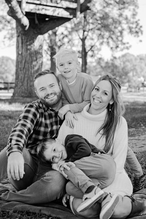 Black and white portrait of happy family of four relaxing under a large tree outdoors.