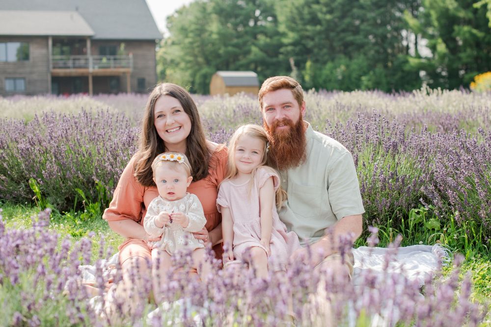 Family of four sitting in a lavender field, smiling at camera on a sunny day.