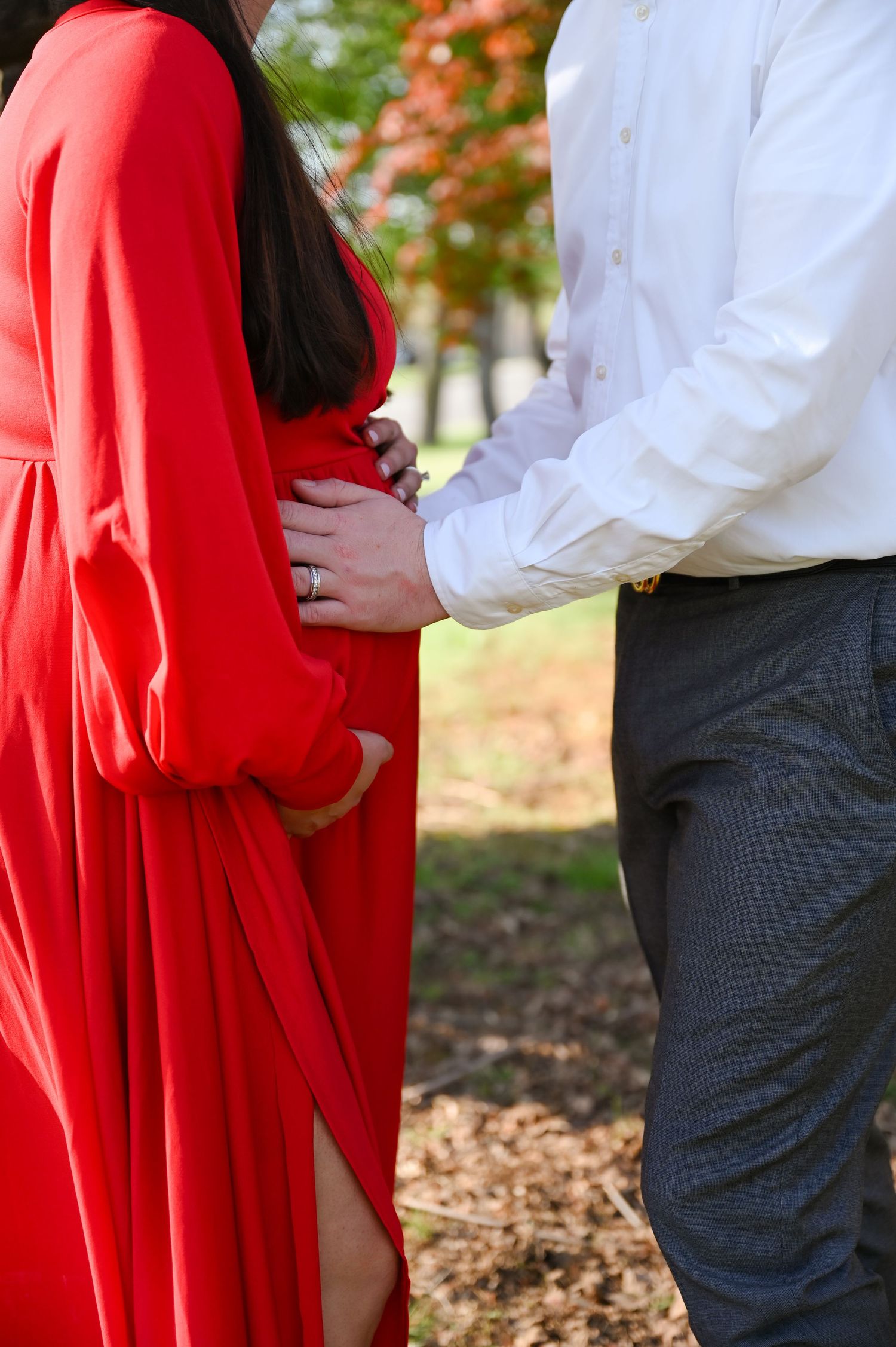 Maternity photo showing couple in red dress and white shirt outdoors during autumn.