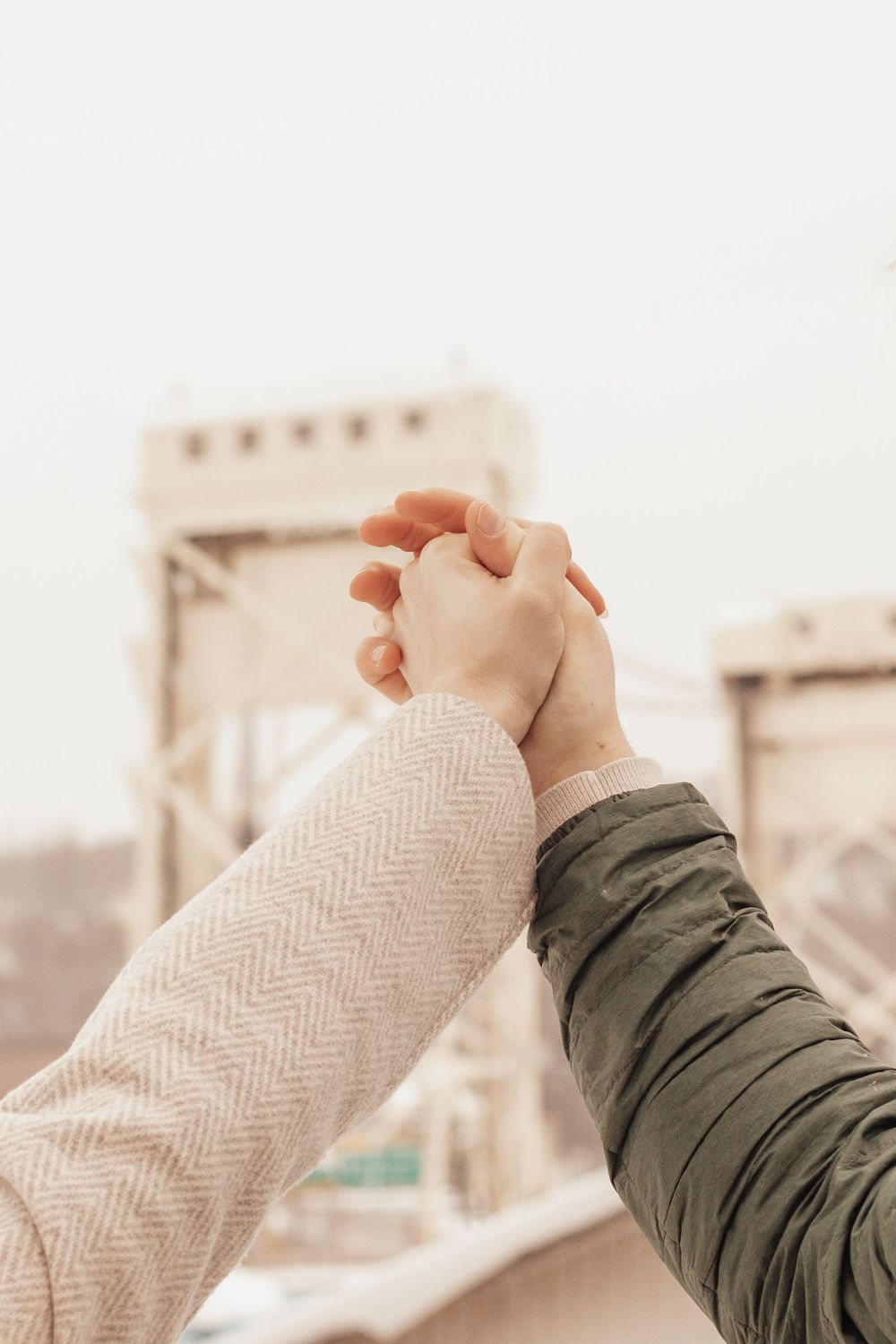 Close-up of intertwined hands with bridge towers visible in background.