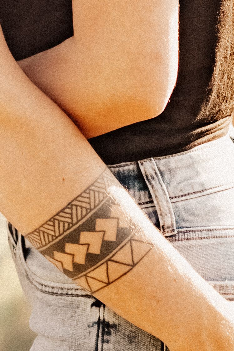 Close-up of a geometric tribal tattoo design on an arm with denim jeans.