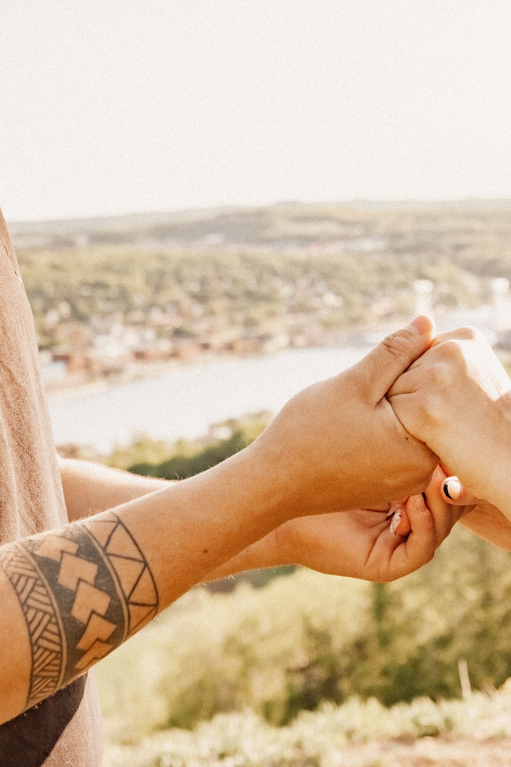 Hands clasped together with a geometric tattoo visible against a scenic landscape backdrop.