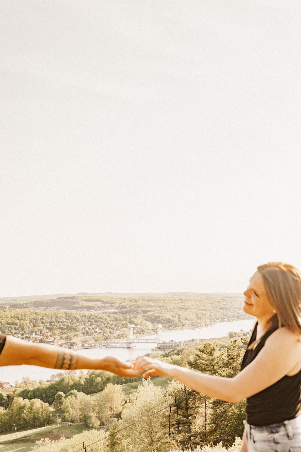 Two people holding hands while overlooking a scenic river valley at sunset.