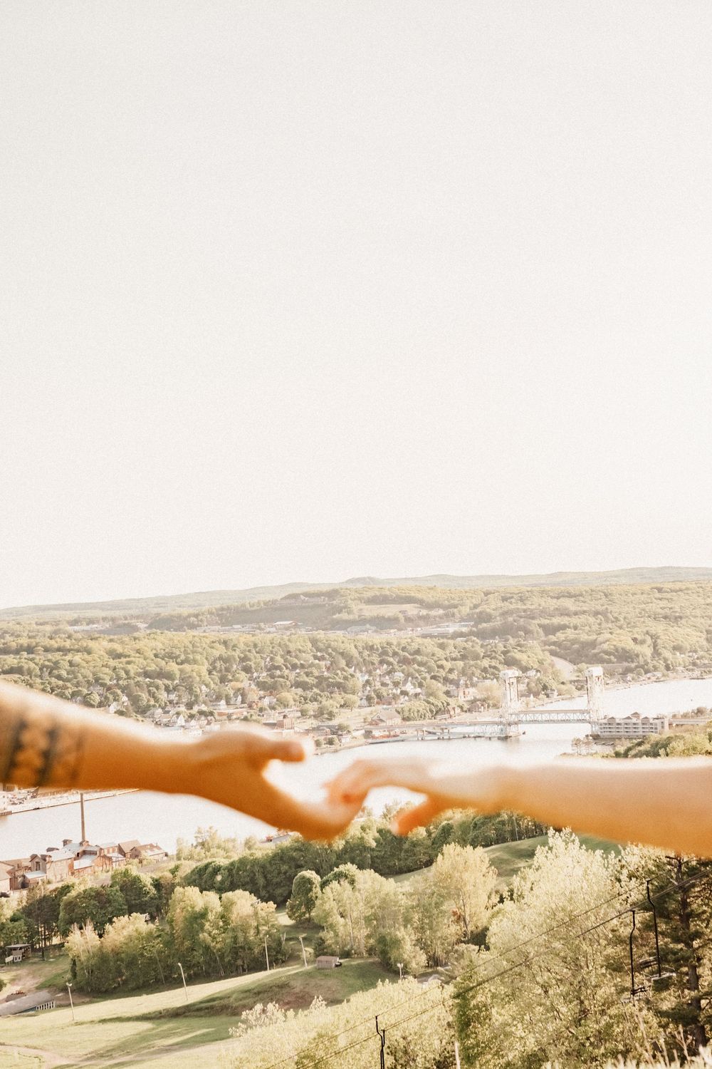 Outstretched arms pointing towards a scenic valley town view in golden sunlight.