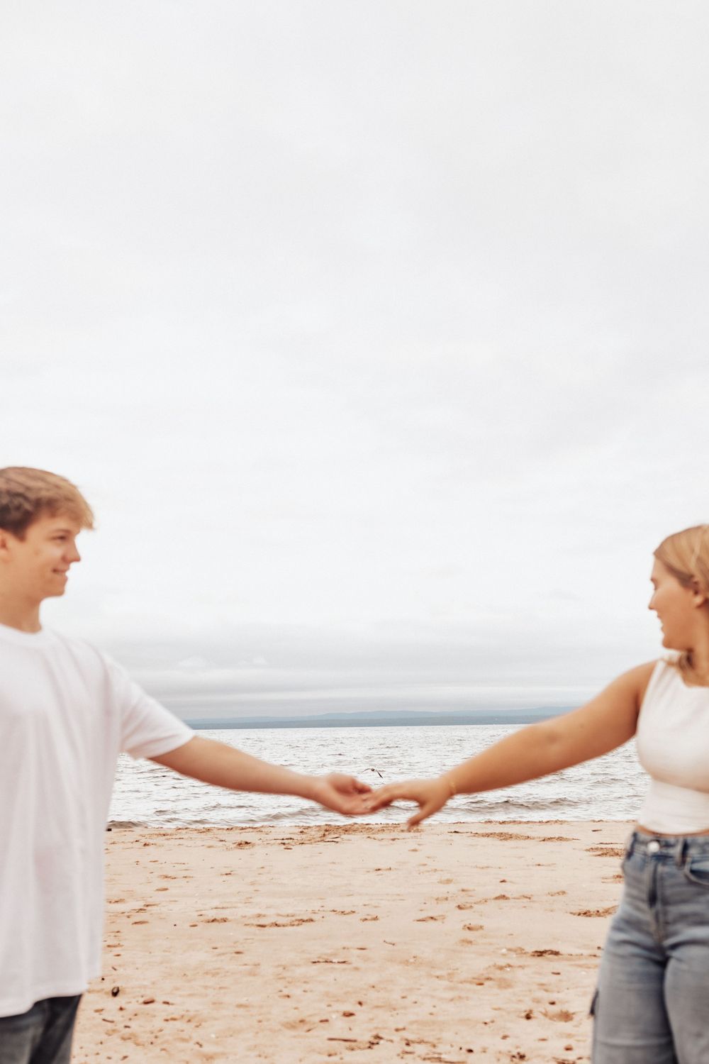 Close-up view of two people holding hands while walking together on a sandy beach by the ocean.