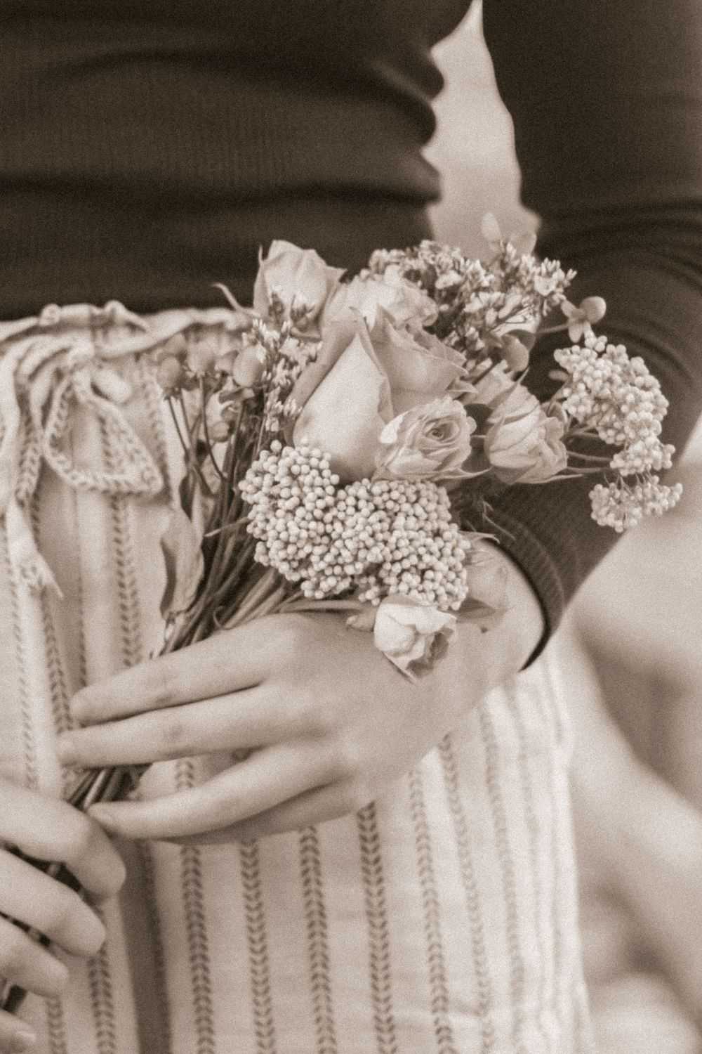 Close-up of hands holding a romantic bouquet with roses and baby's breath in sepia tones.