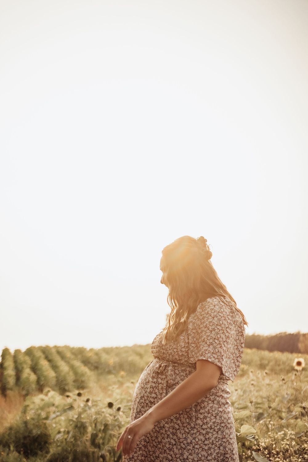 Silhouette of a pregnant woman in a floral dress standing in a sunlit field.