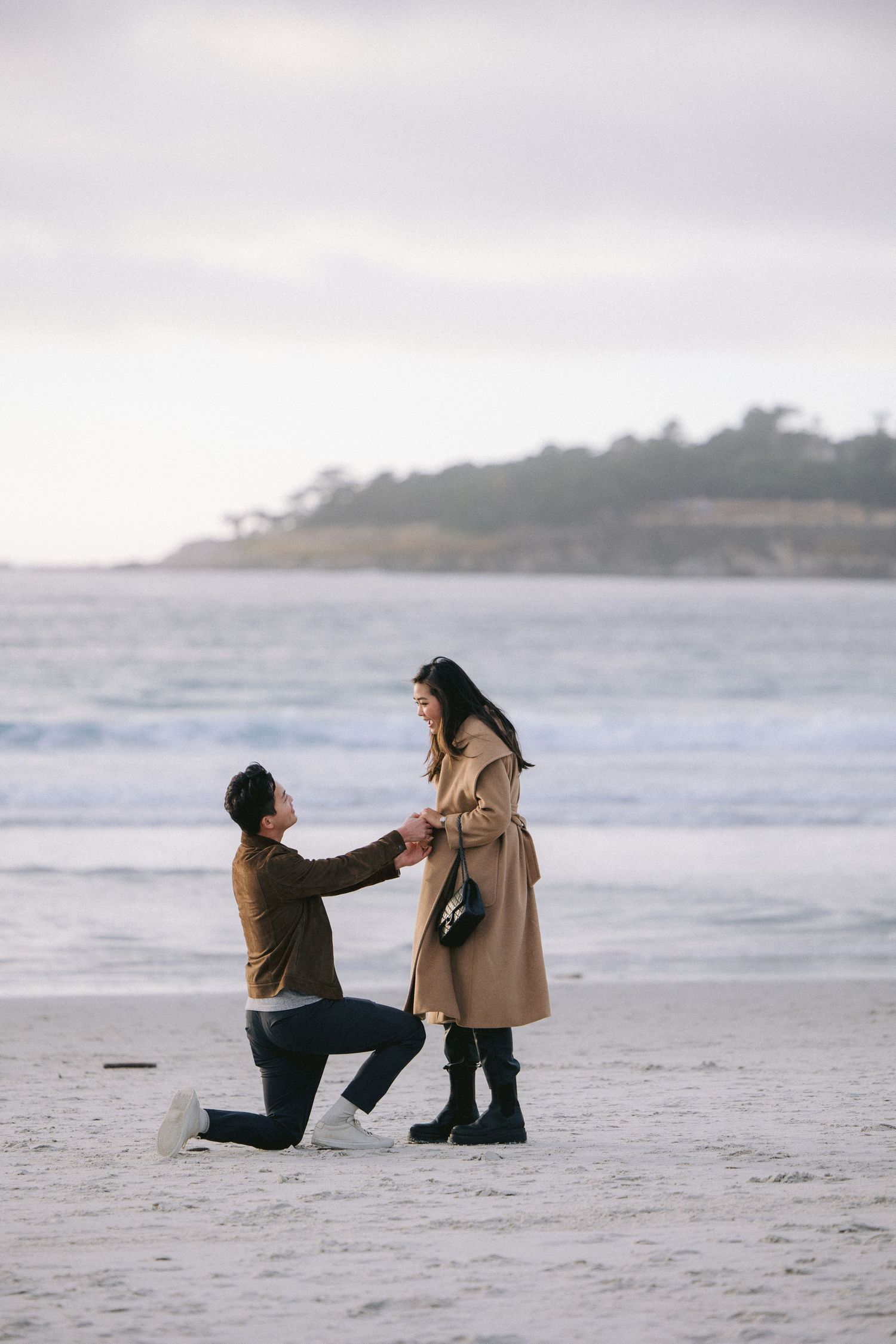A romantic beach proposal scene with coastal cliffs in the background during an overcast day.