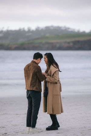 Two people sharing an intimate moment during a beach proposal with coastal cliffs in the background.