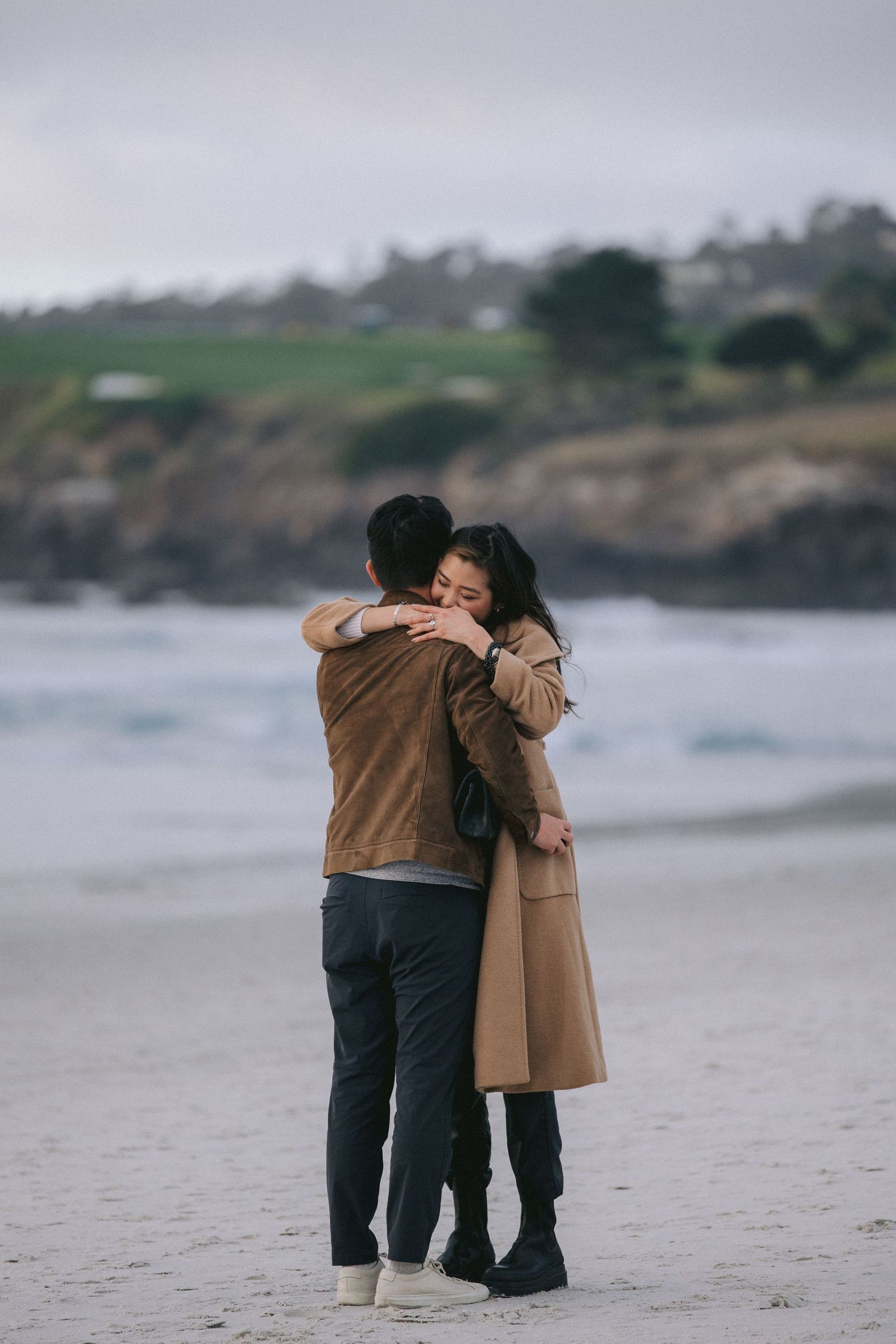 A couple embracing on a misty beach after a proposal with dramatic coastal cliffs in the distance.