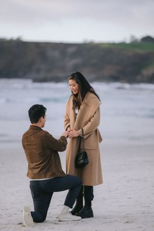A romantic marriage proposal scene on a misty beach with cliffs in the background.