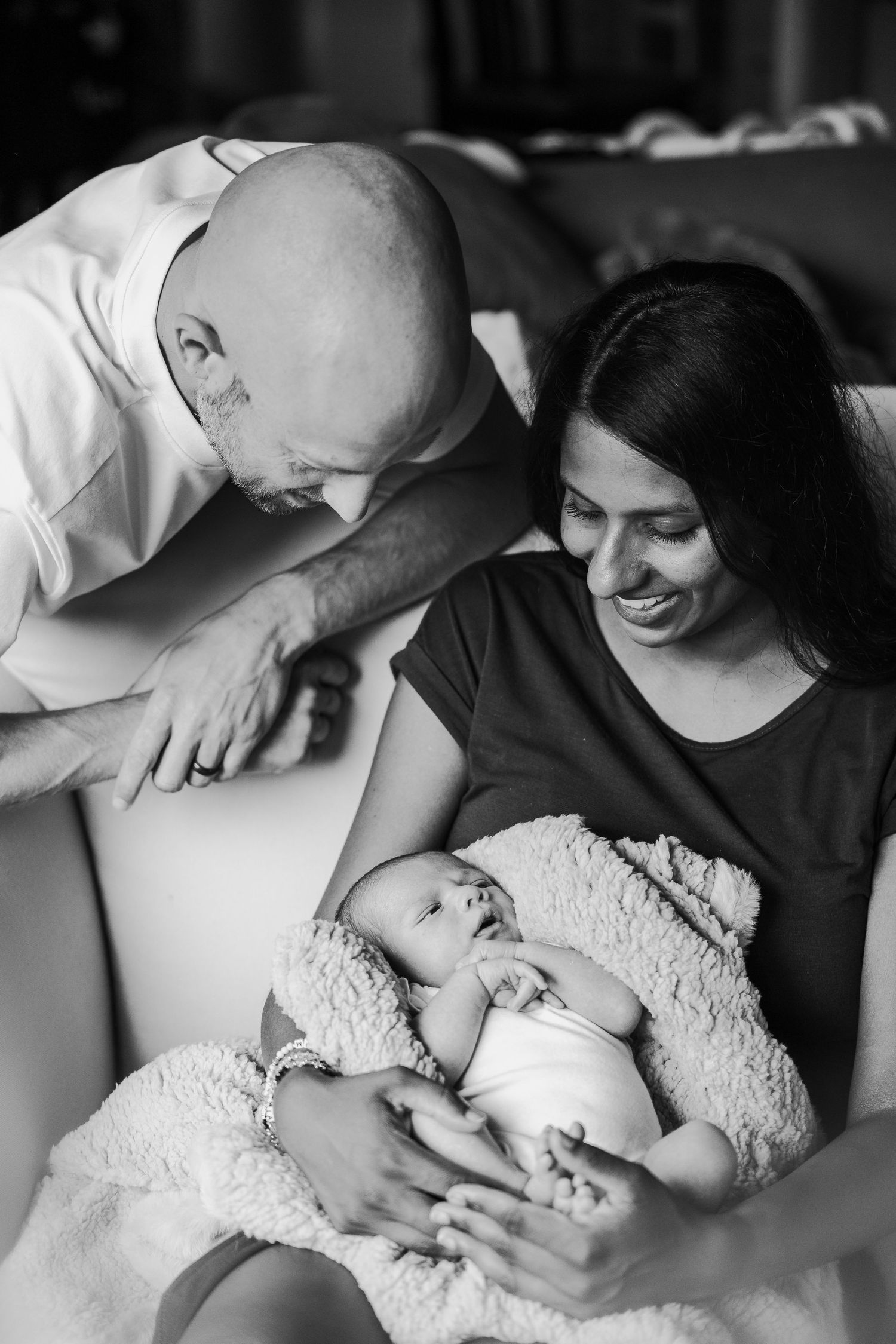 Black and white photo of loving parents gazing adoringly at their sleeping newborn baby swaddled in lace.