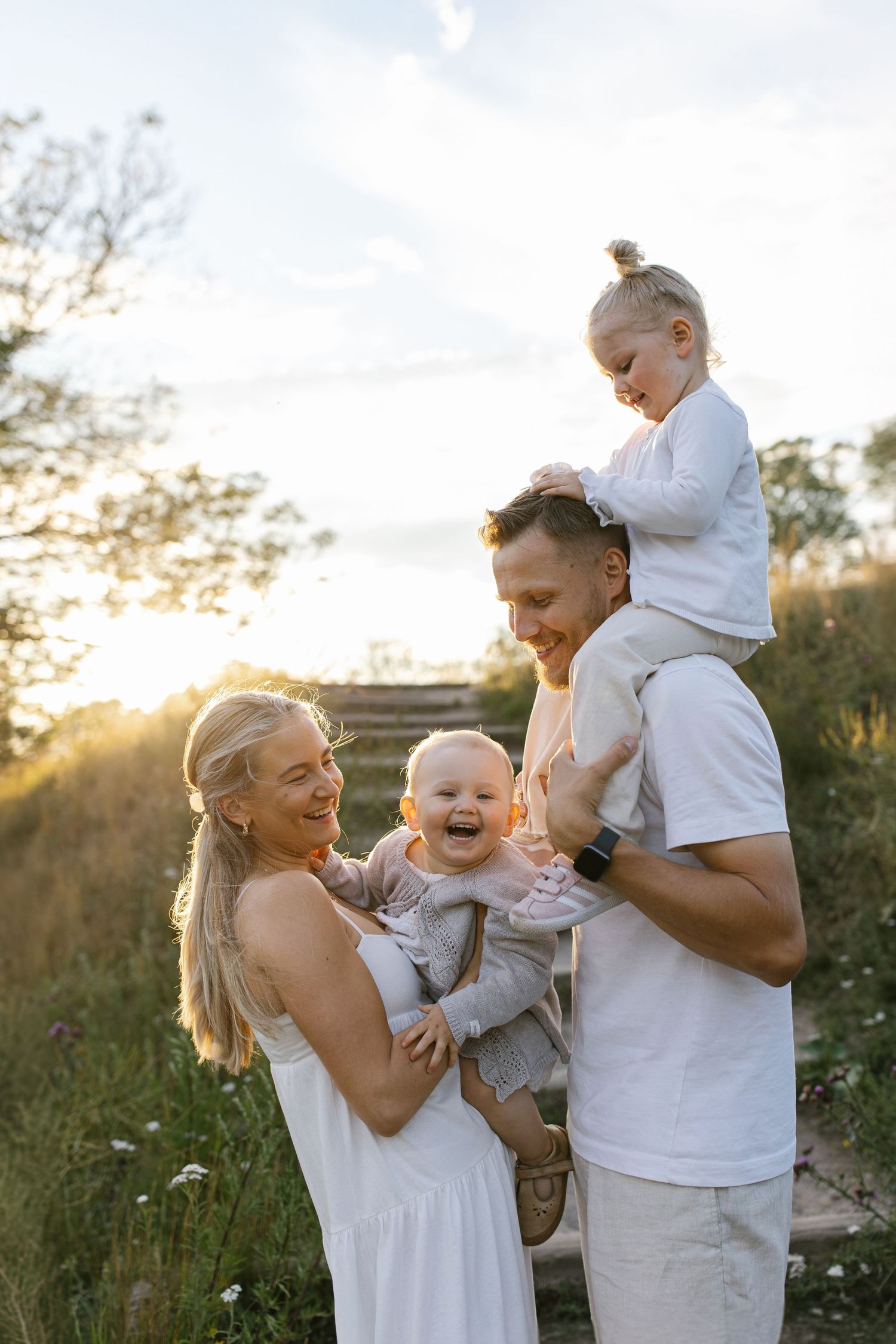 A family enjoys a tender moment together outdoors during golden hour sunset in a natural field setting.