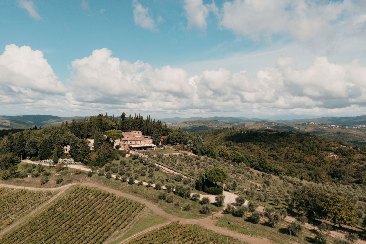 Aerial view of a Tuscan villa surrounded by vineyards and olive groves on a hillside.