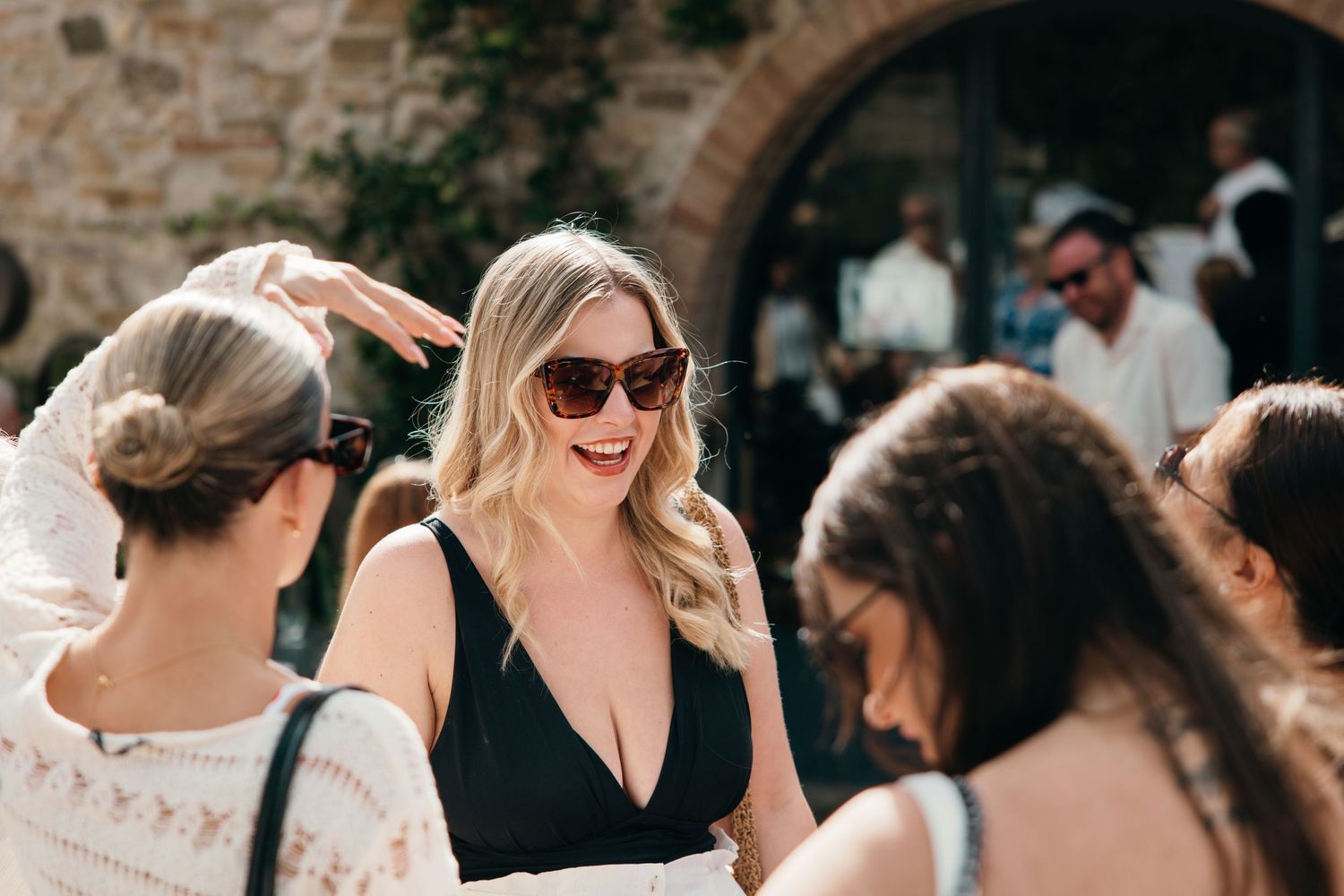 Group laughing together at outdoor gathering with stone wall backdrop.