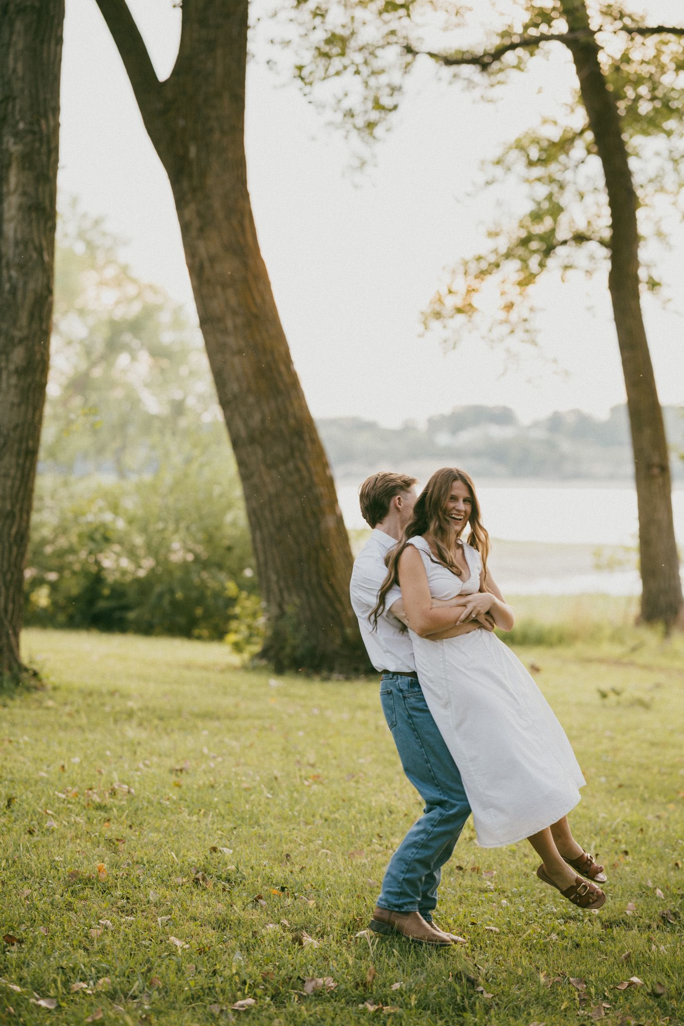 Couple dancing together on a wooden deck during sunset with bare tree branches in background.