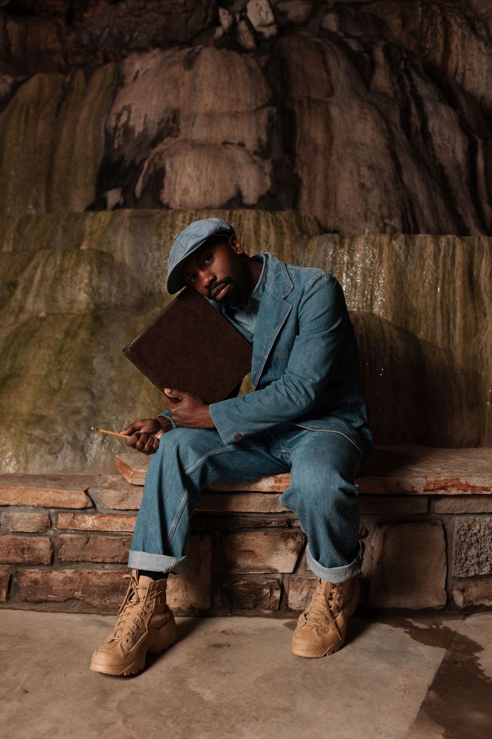 A figure in denim clothing and tan boots sits on a stone ledge, creating a mood of solitude and reflection.
