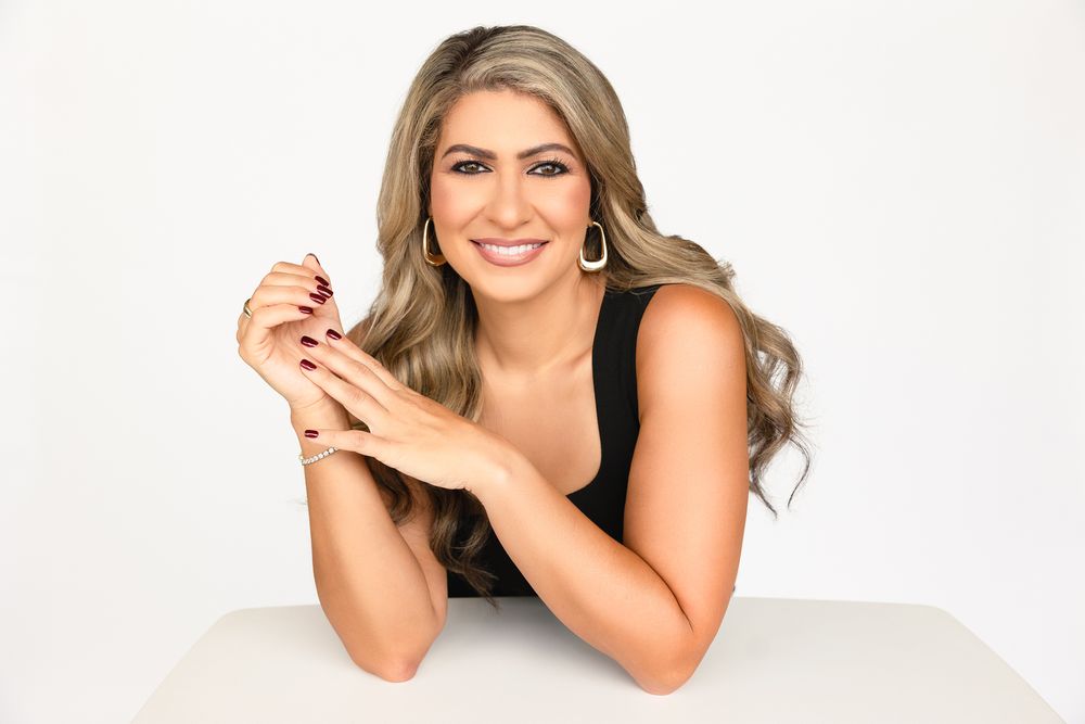 Professional studio portrait of someone lying on a white backdrop wearing a sleeveless top and smiling warmly.
