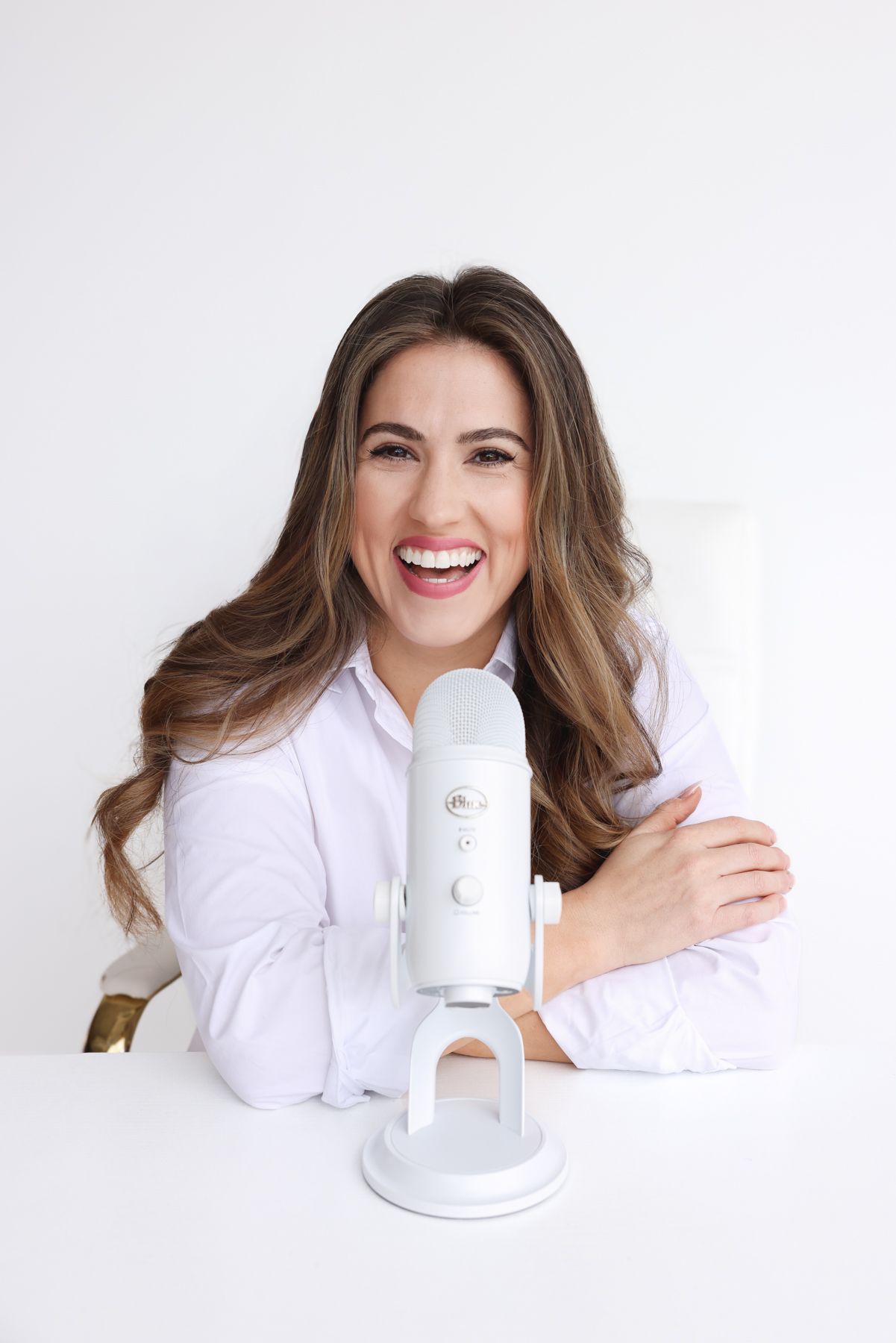 Professional content creator smiles while recording audio content with a white microphone at a minimalist desk setup.