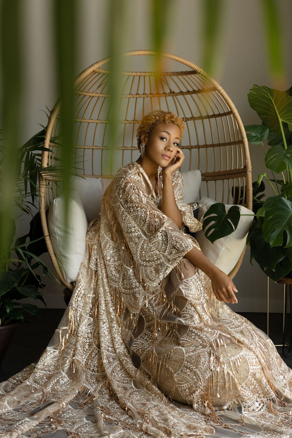 Artistic portrait in lace dress sitting in egg chair surrounded by tropical plants.
