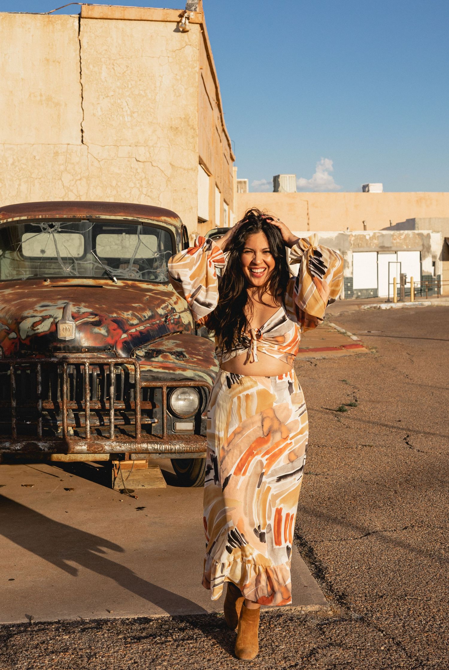 Fashion portrait by vintage truck wearing flowy patterned dress in desert setting.