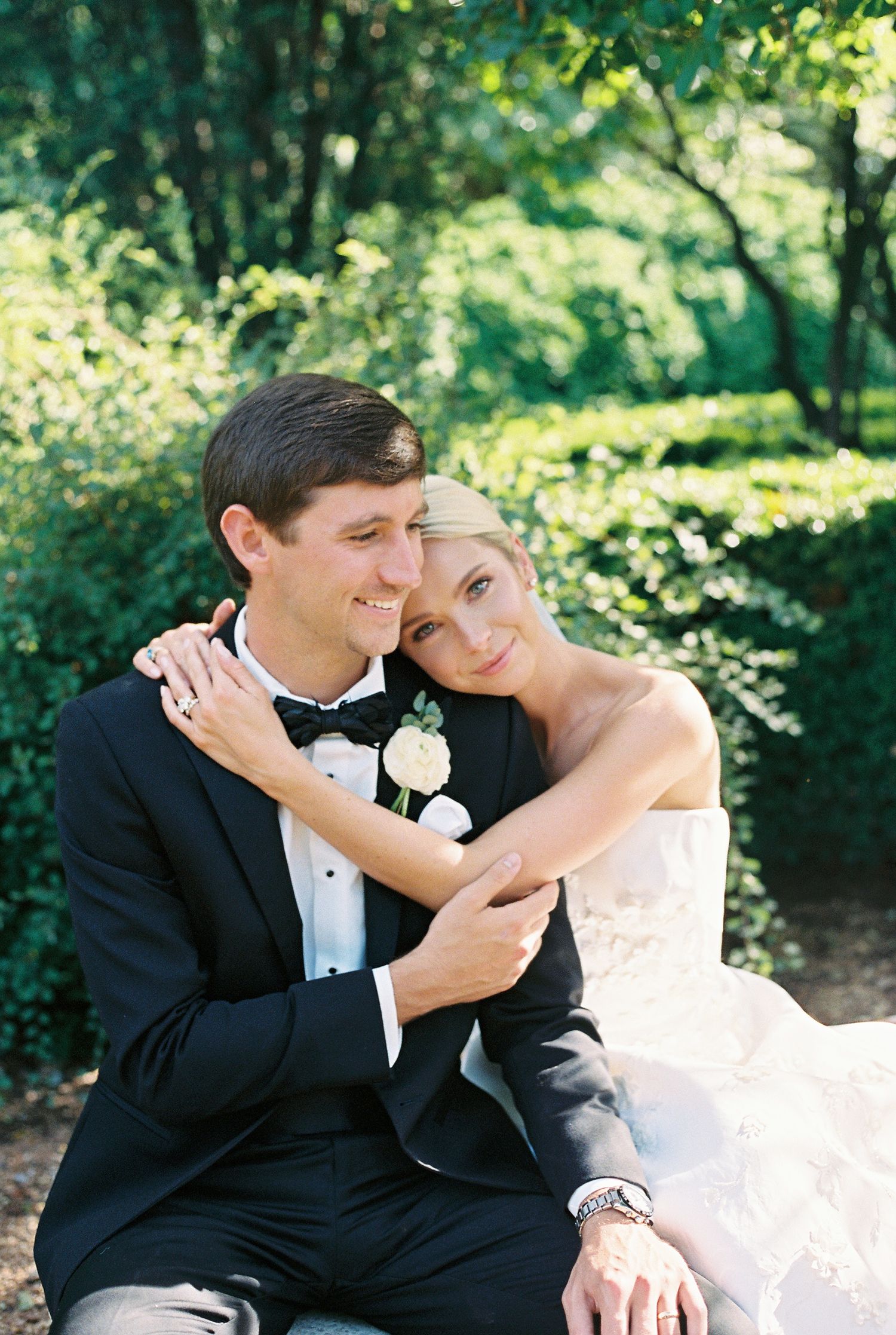 A couple in wedding attire sharing an intimate moment outdoors in a sunlit garden setting.