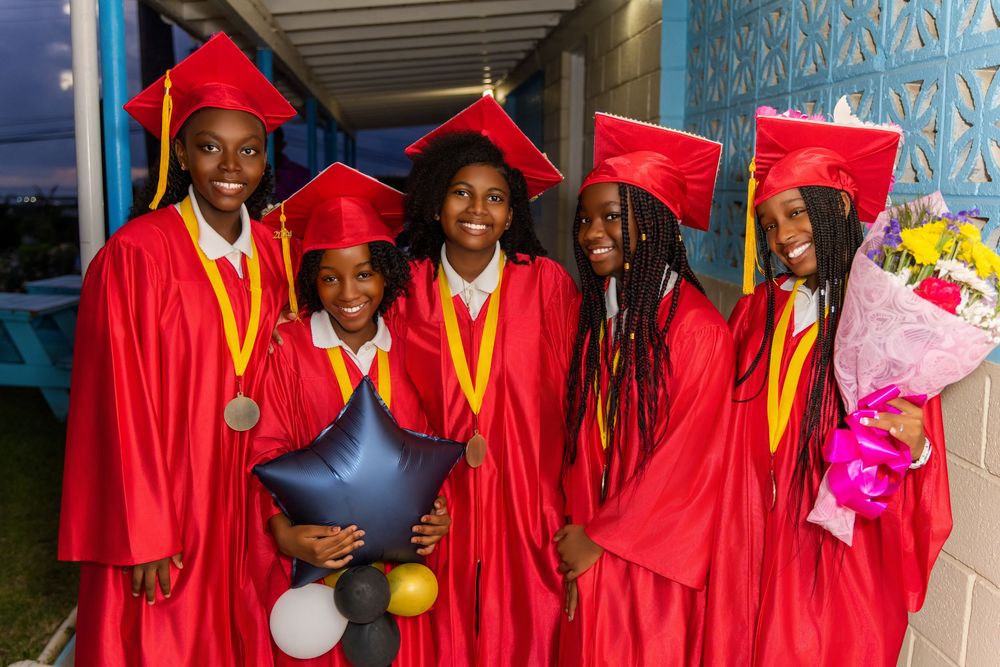 Graduates in bright red caps and gowns with yellow stoles celebrate together holding balloons and flowers on graduation day.