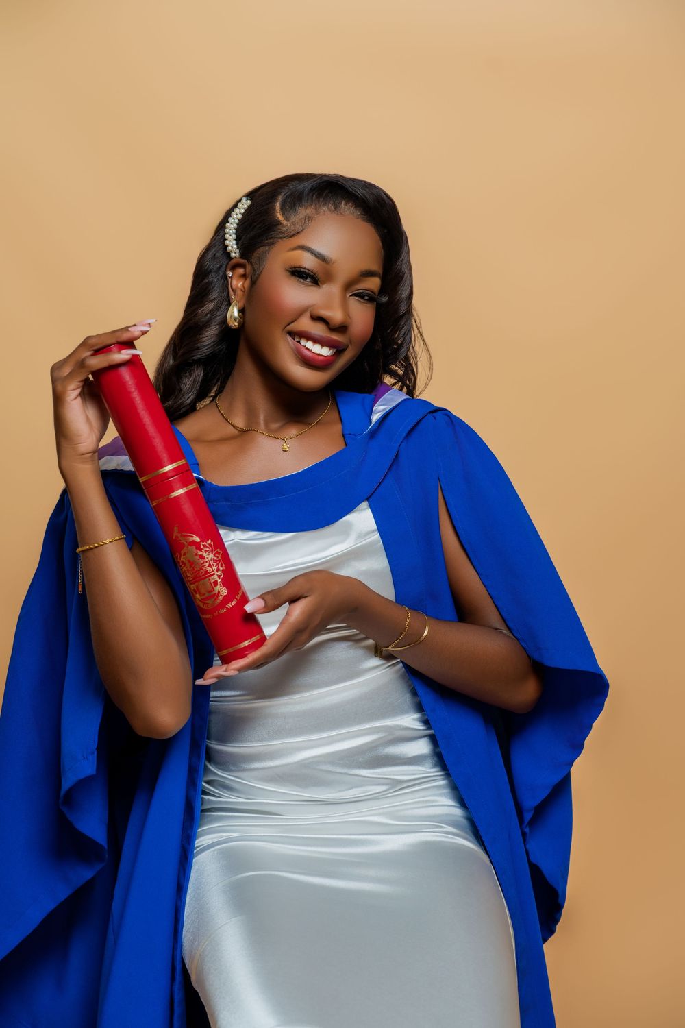 A person in a royal blue blazer and silver dress poses with a red decorative cylinder against a beige background.