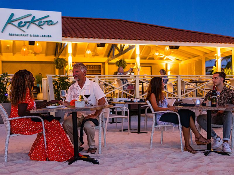 Diners enjoy outdoor seating at Koko's restaurant with warm lighting and a red roof during twilight hours.