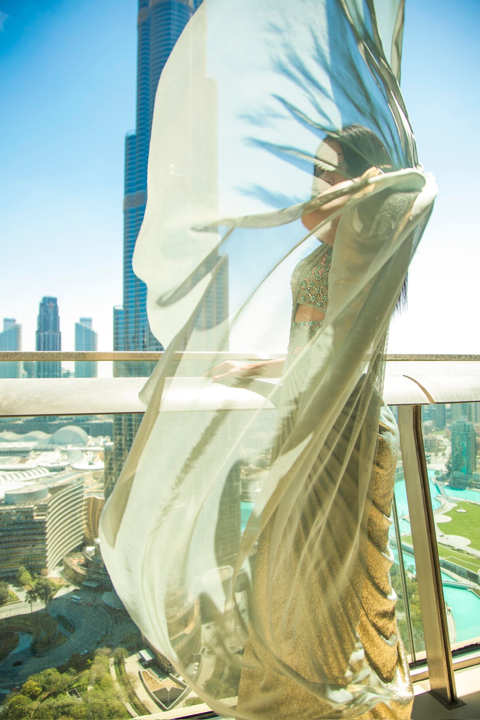 Woman in flowing white outfit on balcony with Burj Khalifa skyline backdrop in Dubai.