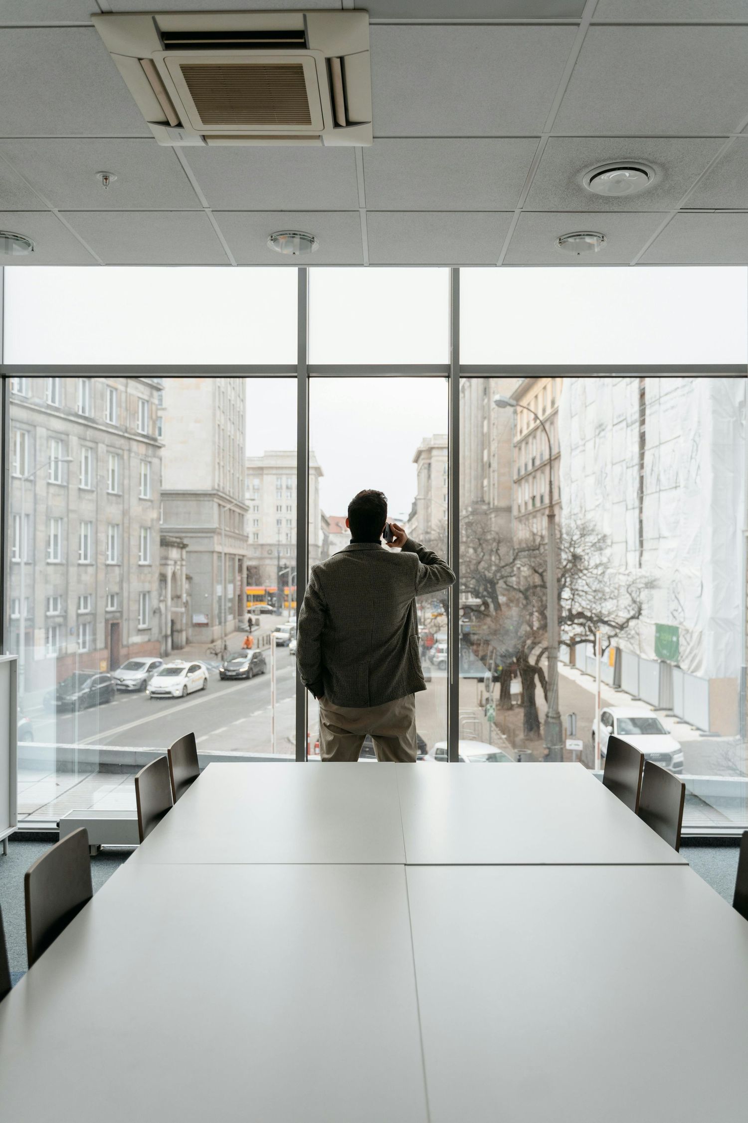 Business professional standing at a conference room window overlooking a snowy city street in winter.