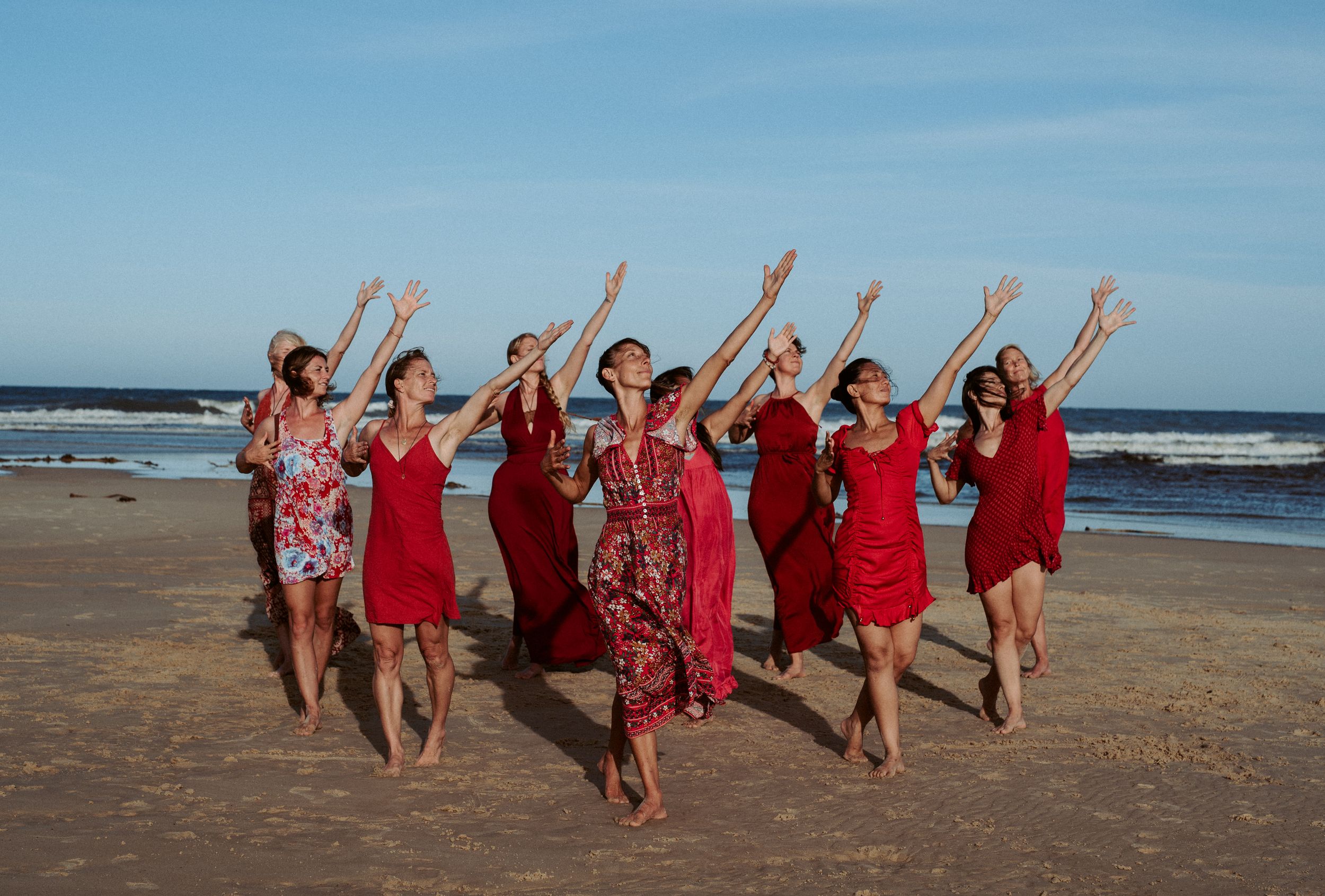 A celebratory group in red dresses poses and dances along the shoreline.