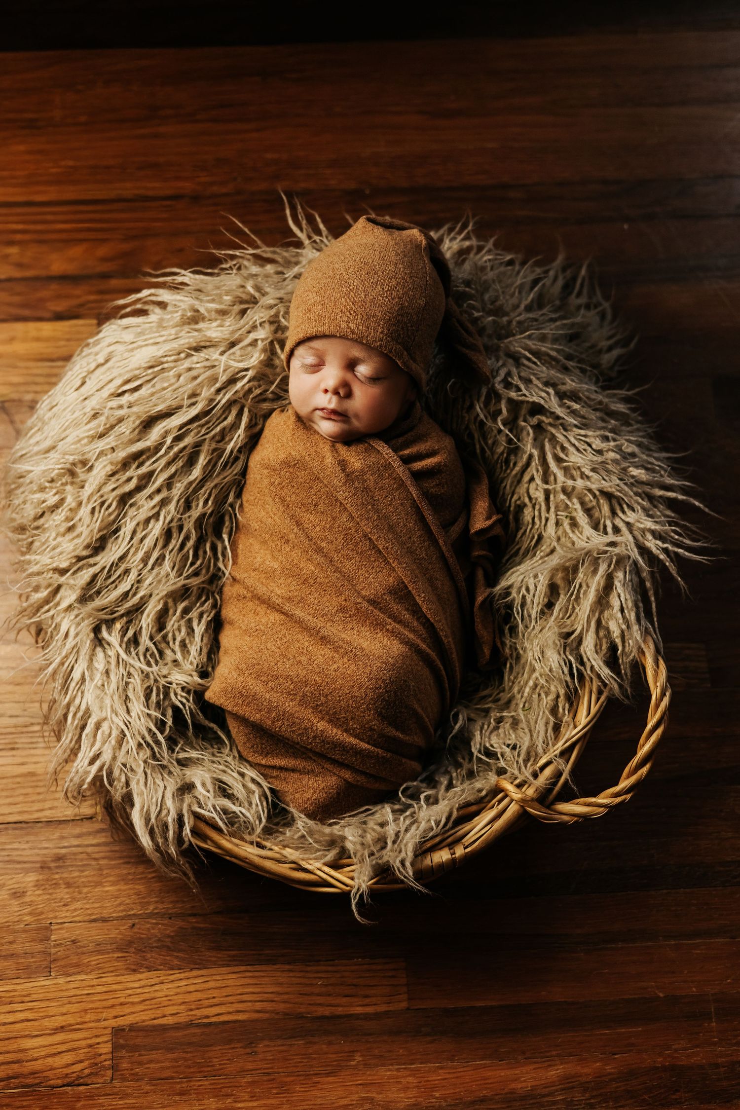 Artistic newborn portrait on wooden floor with textured fur backdrop.