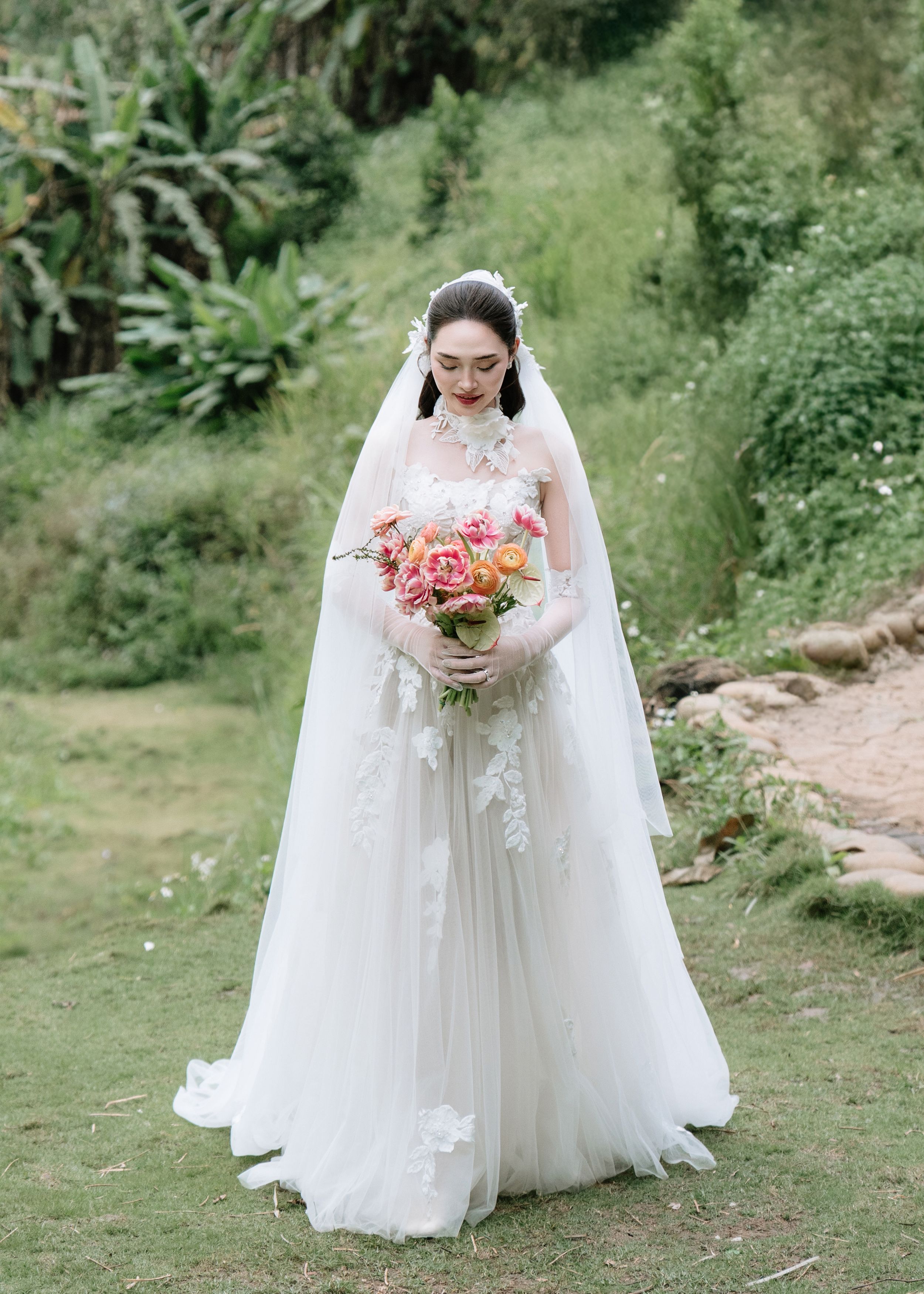 Elegant bride in white tulle gown with veil holding colorful bouquet outdoors.