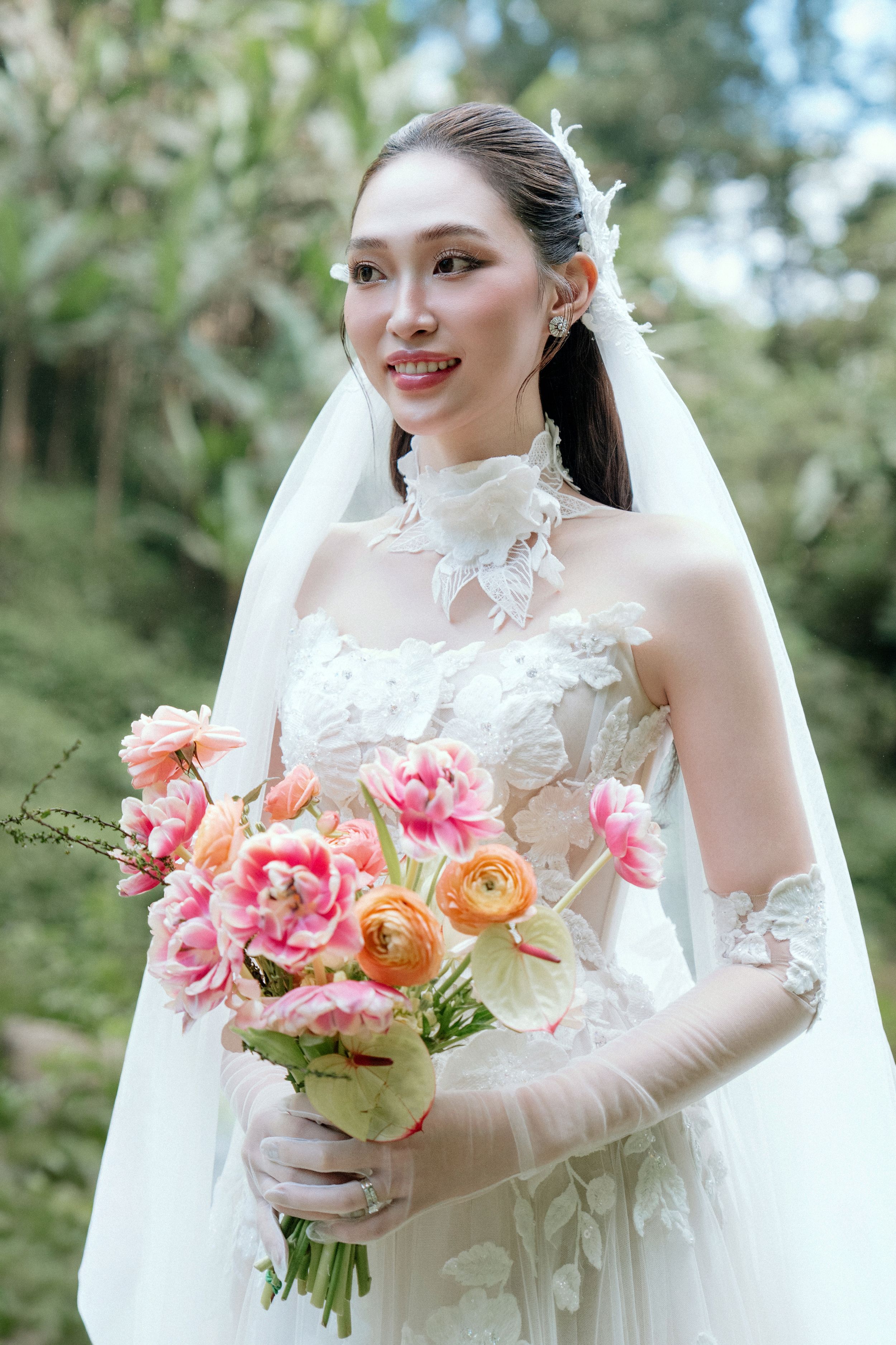 Smiling bride in lace wedding dress holding pink and orange floral bouquet.