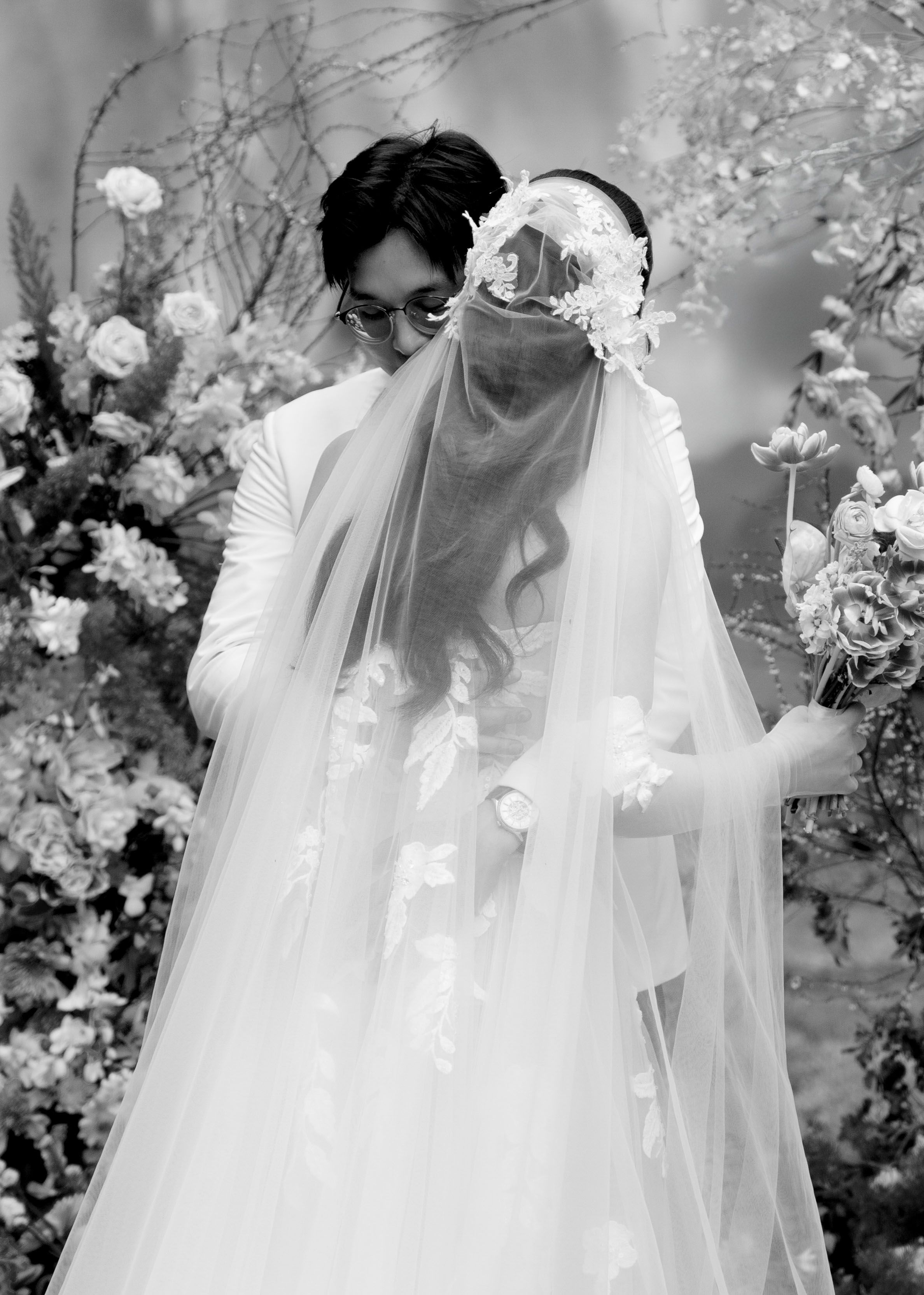 Black and white photo of groom kissing bride through her floral wedding veil.