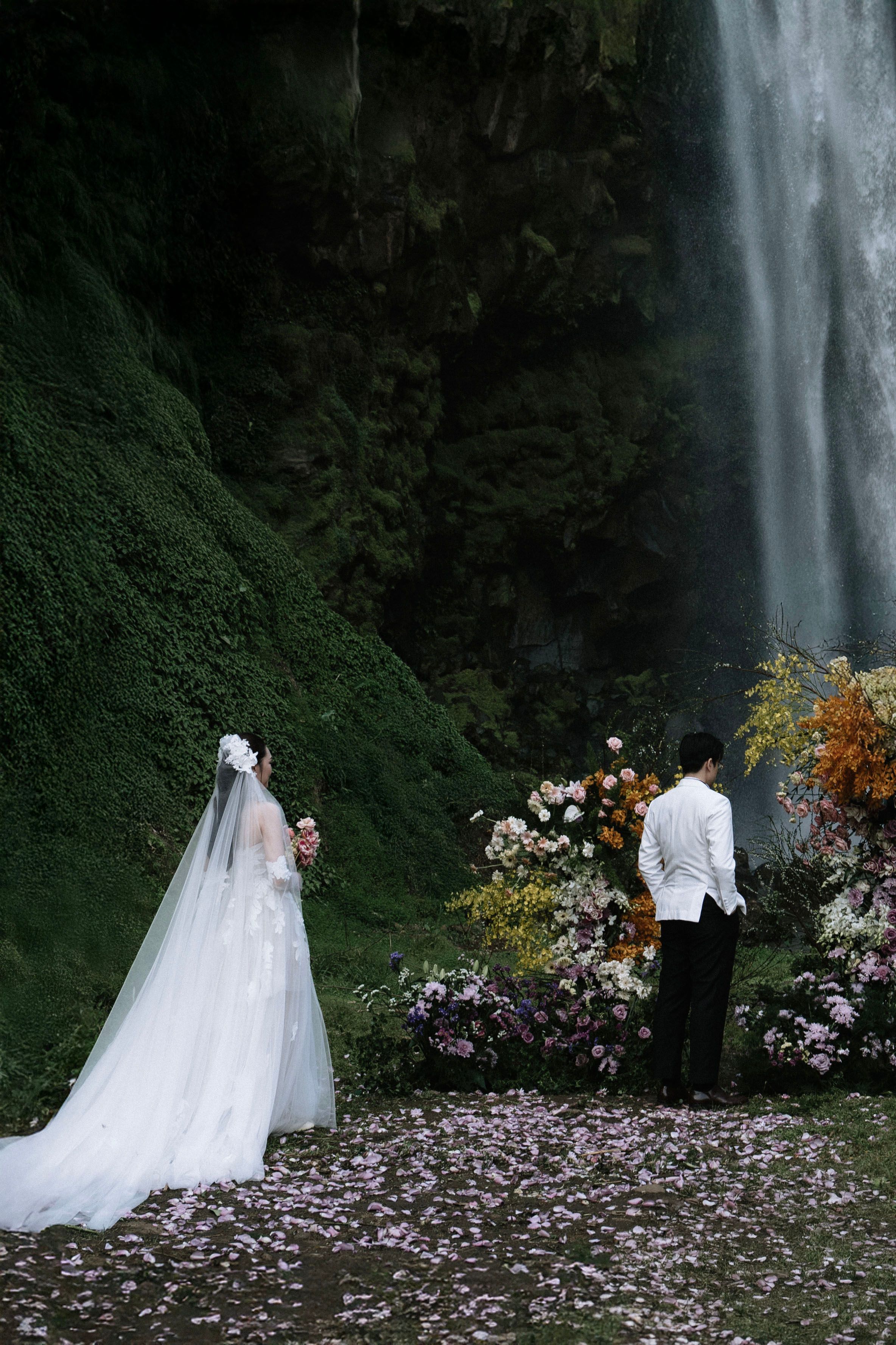 Bride and groom standing before stunning waterfall altar adorned with colorful floral arrangements.