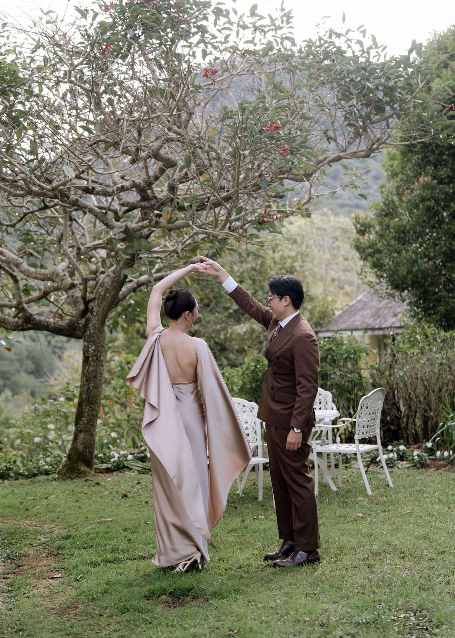 Couple dancing elegantly in a lush garden with scenic mountain backdrop.