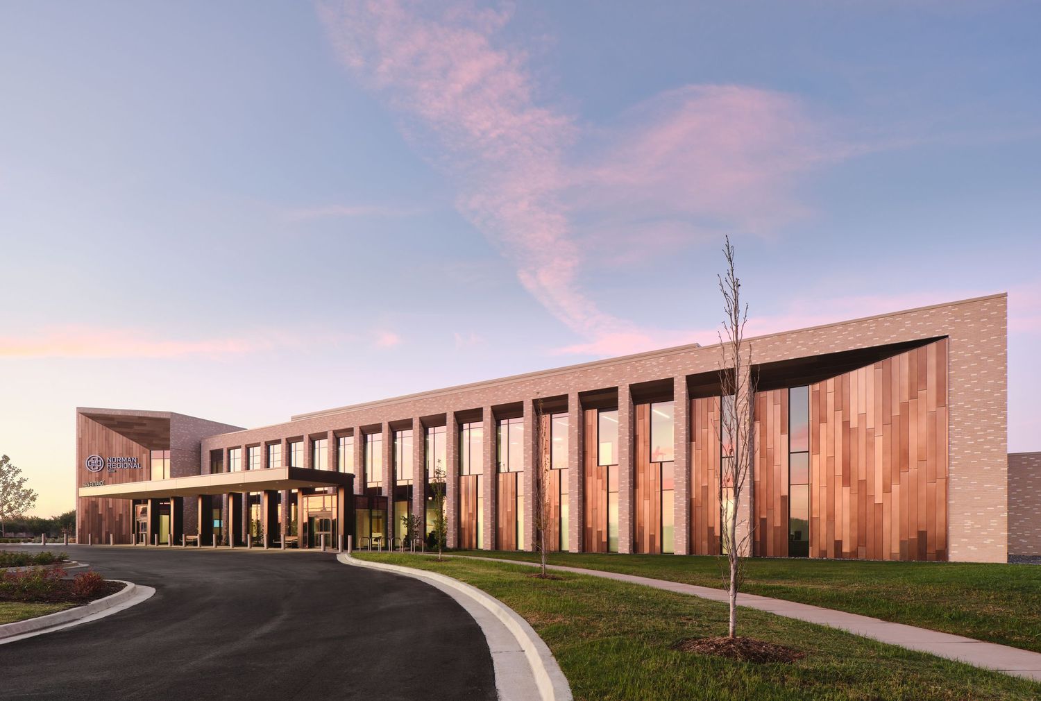 Modern office building with copper-colored metal exterior panels under pink sunset sky at dusk.
