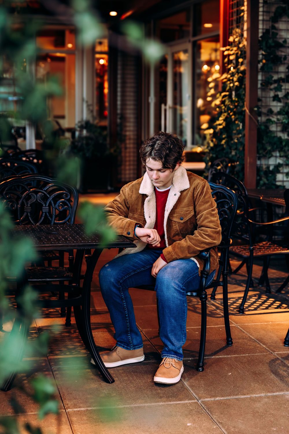 Person relaxing on outdoor patio bench wearing brown jacket and red sweater.