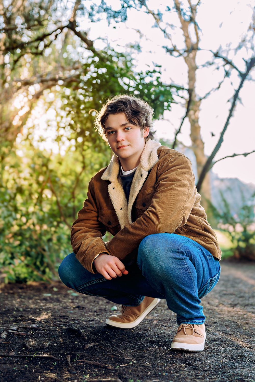 Casual outdoor portrait session in brown jacket against natural sunset backdrop.